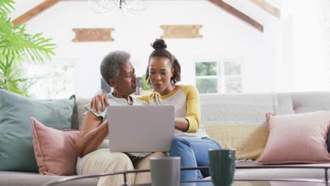 African-american-mother-and-daughter-smiling-while-using-laptop-together-at-home