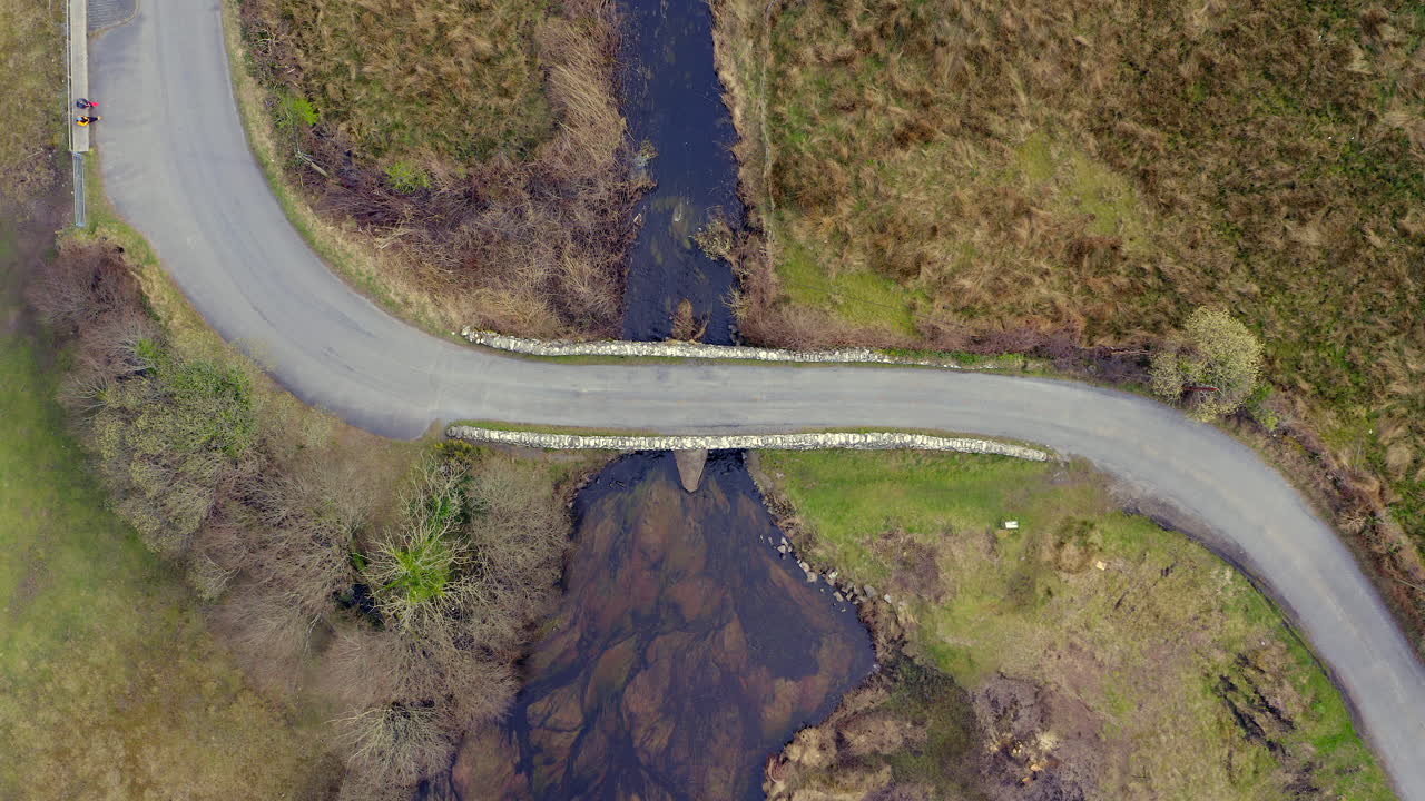 Aerial descent showcasing the iconic Quiet Man Bridge nestled among Connemara's verdant countryside and winding streams.