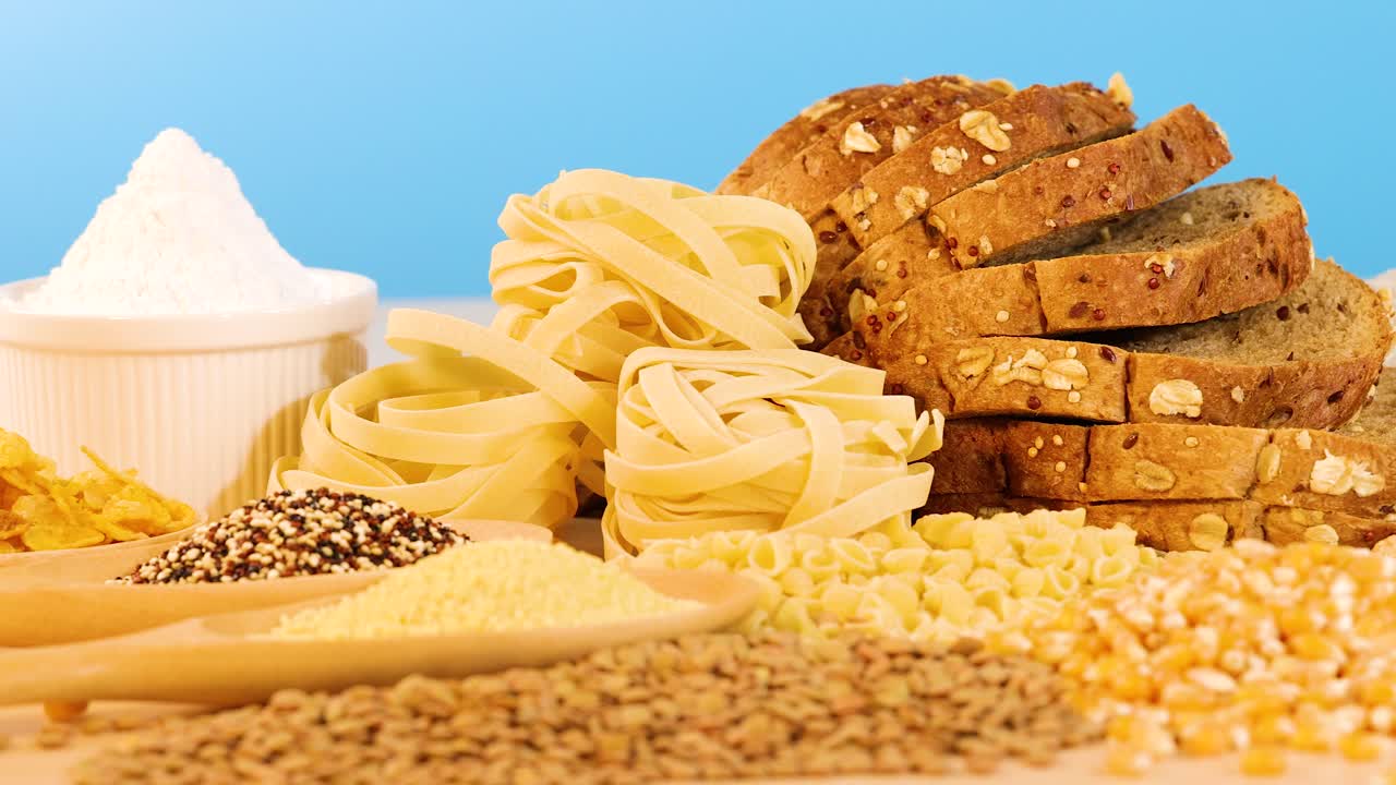 A variety of grains, pasta, and bread arranged against a bright blue background, highlighting textures and colors