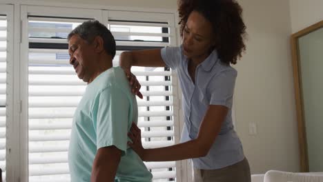 Physiotherapeutin-Gemischter-Abstammung-Hilft-Einem-älteren-Mann,-Seinen-Rücken-Zu-Massieren