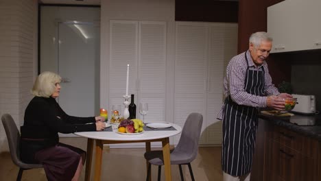 anciano cocinando para su esposa una cena romántica con vino y velas. pareja de ancianos enamorados