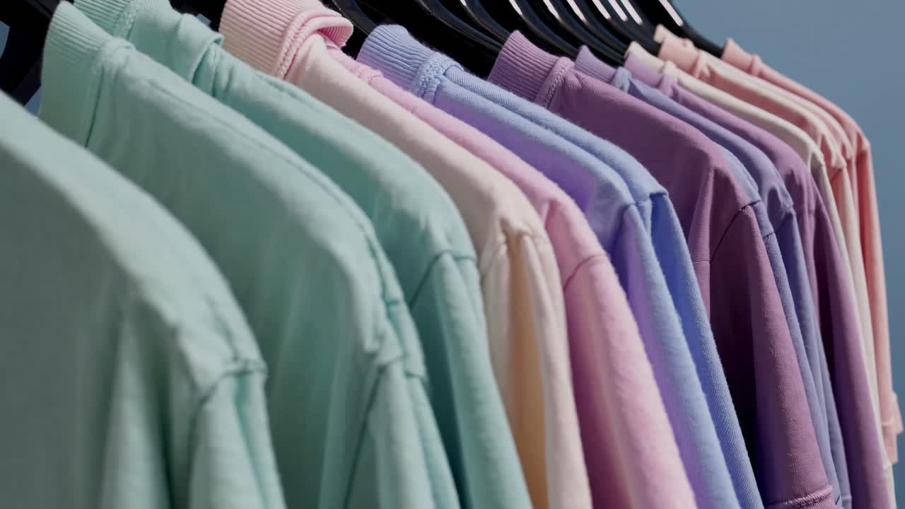 Una fila de camisetas pastel en perchas, capturada desde un ángulo lateral.