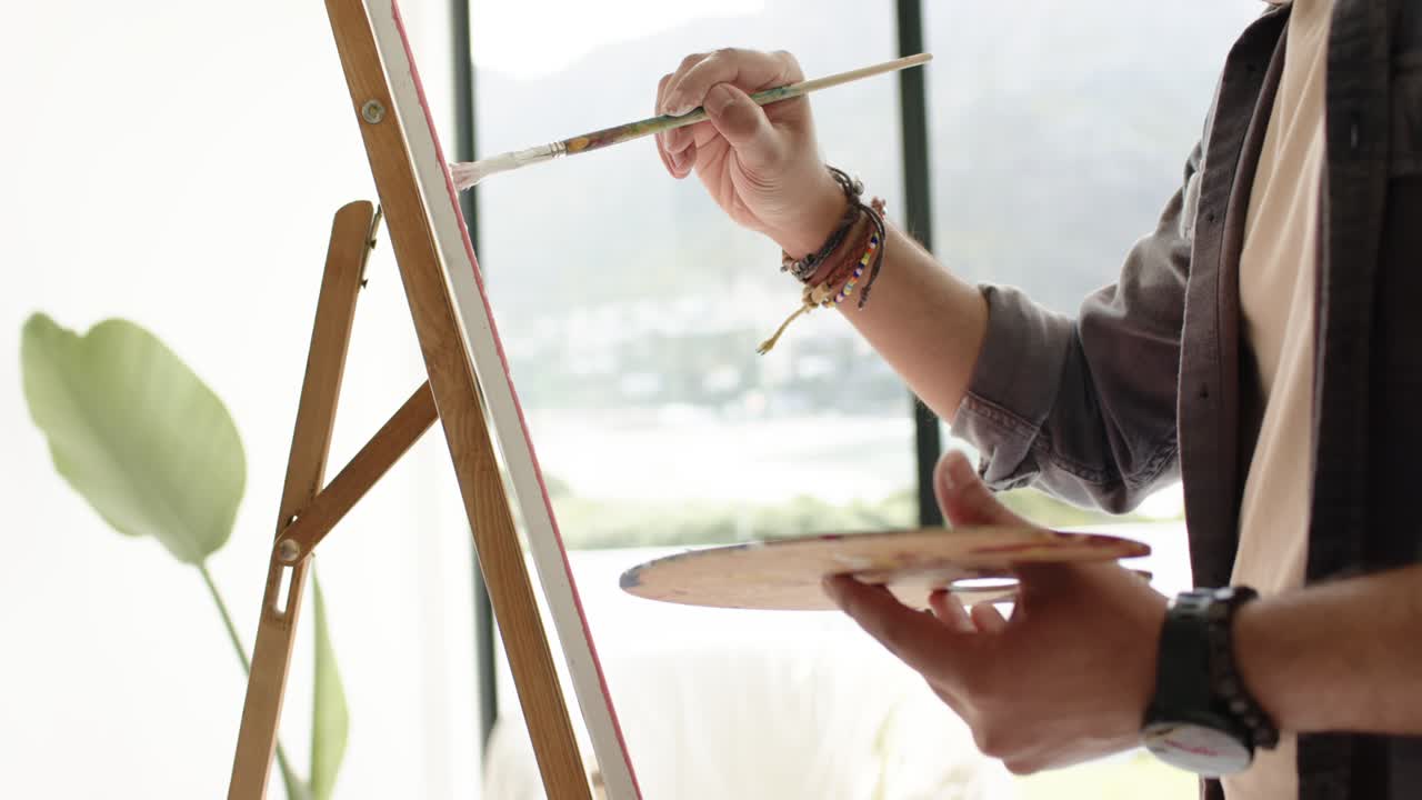 After dipping brush in red paint, painter's hands are outlining canvas on easel finishing border