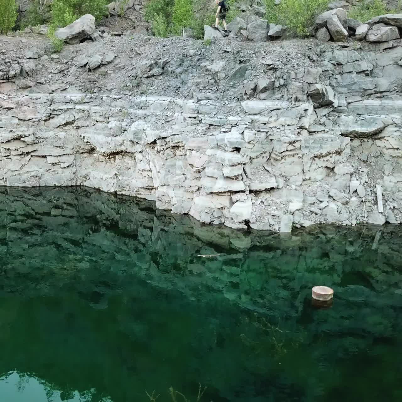 Aerial view of a young traveler with a backpack walking along a rocky path. Rocky shoreline of the lake with forest. Camping season
