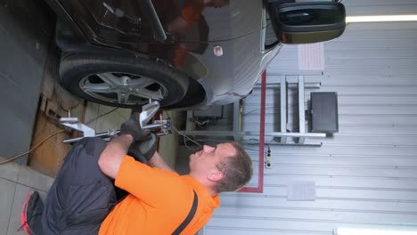 a mechanic performs wheel alignment on a car in an auto service garage