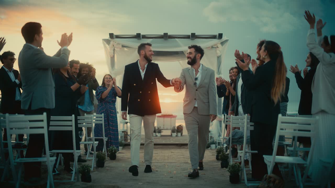 una hermosa pareja gay caminando por el pasillo en el lugar de la ceremonia de bodas al aire libre cerca del mar. dos hombres felices enamorados comparten su gran día con diversos amigos multiétnicos.