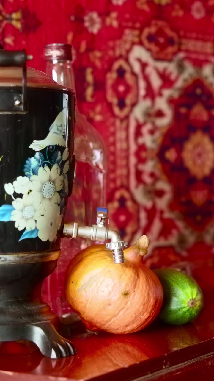 Samovar vintage su tappeto rosso a motivi, urna metallica con decorazioni floreali e rubinetto poggiata su un tavolo di legno
