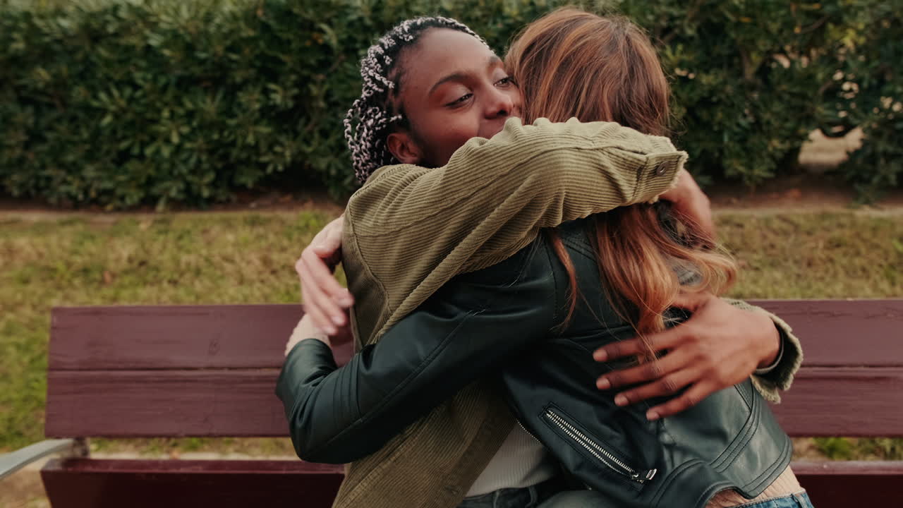 Duas mulheres jovens e diversas se abraçando em um banco de parque