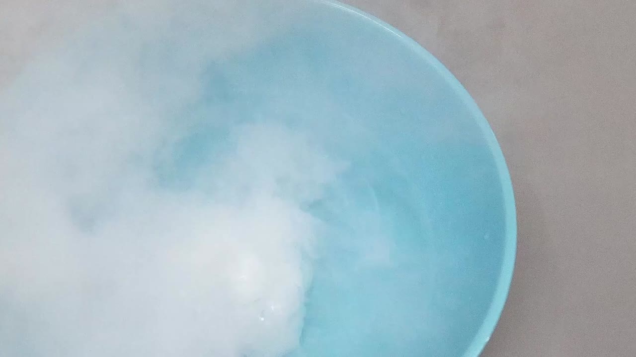 Watch as vapor clouds emerge and swirl in a blue bowl filled with water.