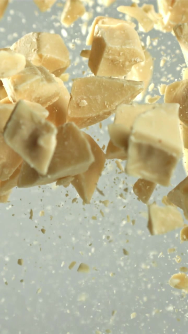 Pezzi di cioccolato bianco che cadono al rallentatore su sfondo chiaro