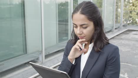 dolly shot of a pensive young business lady using online app on tablet for work while walking outside