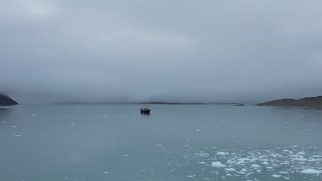 dramatic shot towards an expedition boat in front of a glacier in a cloudy day in a fjord along the coast of the svalbard archipelago