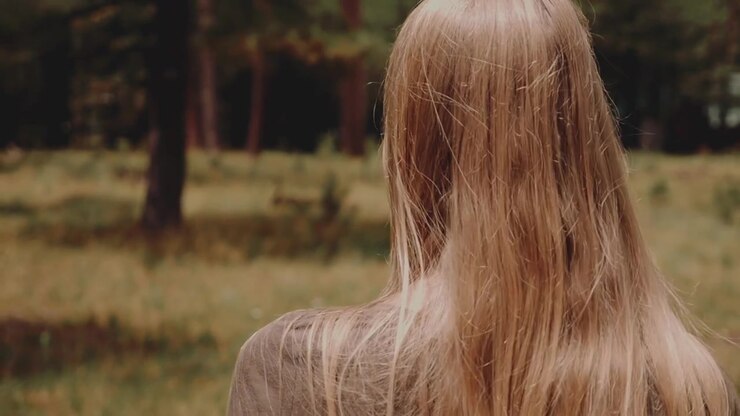 Donna di spalle con lunghi capelli biondi in piedi in una foresta