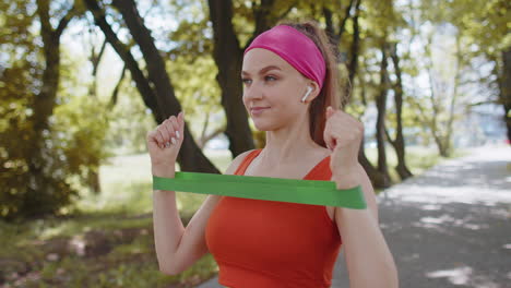 athletic fit sport girl doing hands exercises using fitness elastic rubber band, workout, outdoors