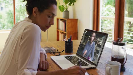 Mujer-Afroamericana-Tomando-Notas-Mientras-Realiza-Una-Videollamada-Con-Un-Colega-Masculino-En-Una-Computadora-Portátil-En-Casa