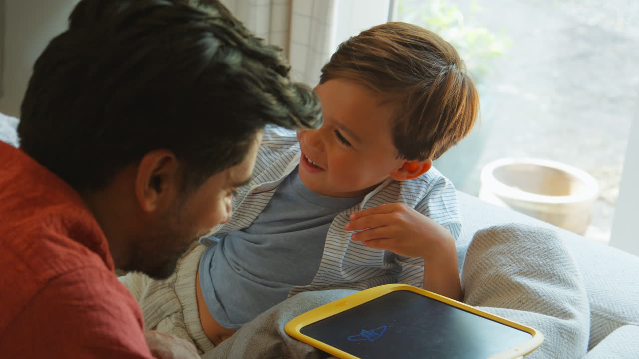 padre e hijo en casa en el sofá en el salón hablando y jugando con el juego de dibujo juntos