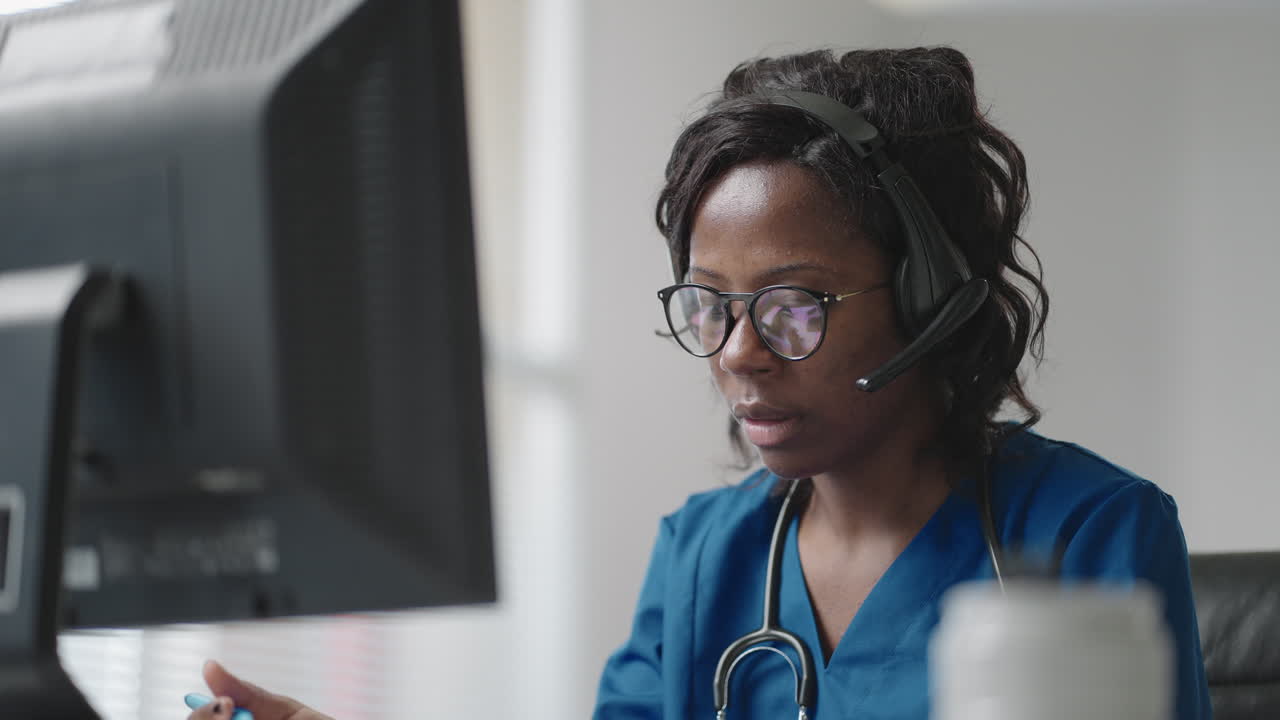 African Female medical assistant wears white coat headset video calling distant patient on computer. Doctor talking to client using virtual chat computer app. Telemedicine remote healthcare