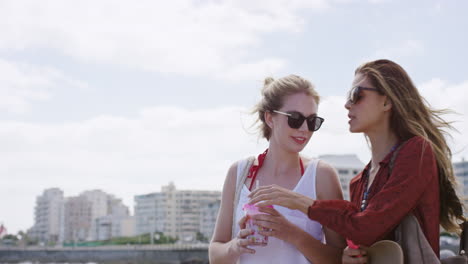 dos chicas amigas compartiendo una bebida caminando por el paseo marítimo de la ciudad costera disfrutando de unas vacaciones relajadas