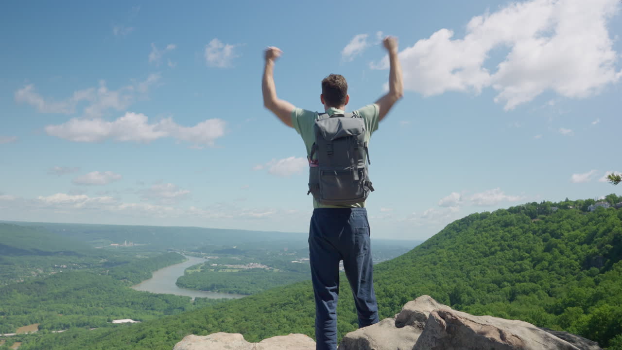 hombre de pie en la cima de un acantilado mirando la vista y levantando los brazos en emoción por su logro y éxito