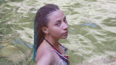 A-young-woman-laying-in-a-river-with-green-curly-hair-on-a-tropical-island