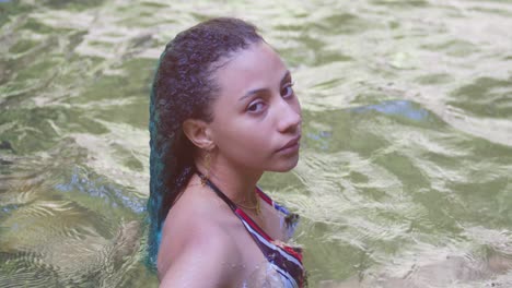 una mujer joven acostada en un río con cabello rizado verde en una isla tropical