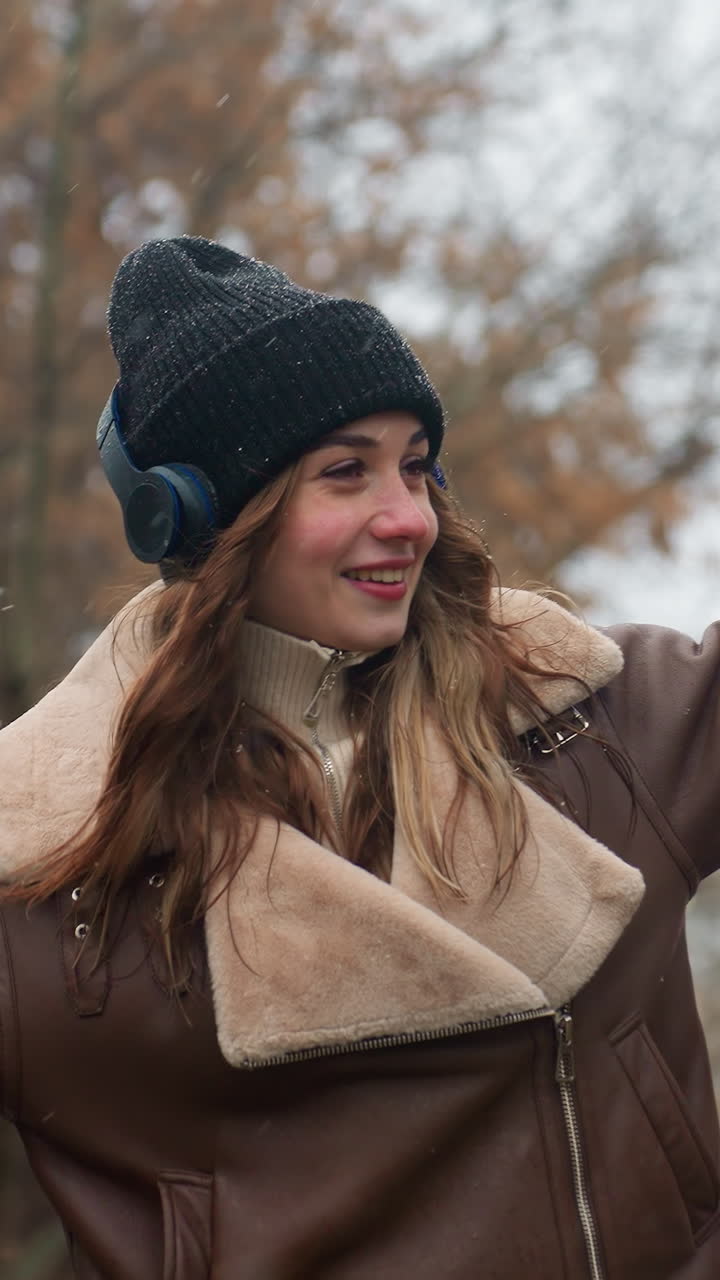 Smiling lady wearing black knit cap, brown shearling jacket with arms outstretched, walking joyfully outdoors on cool autumn day, enjoying nature and fresh air amidst vibrant autumn colors