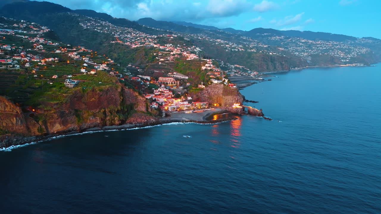 Rocky coast of the Madeira Islands, Portugal with a town dwelling the mountain. Drone footage of the picturesque shore above the waterscape of the Atlantic Ocean.