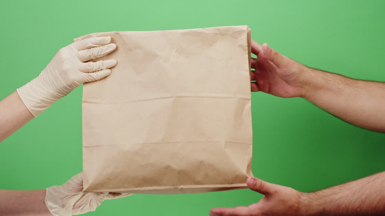 Gloved Hands Delivering a Paper Bag to Another Person on Green Screen