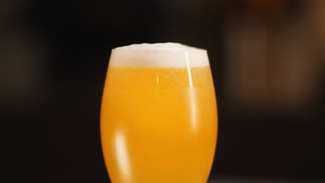 close up of craft beer being poured in to a mostly full goblet beer glass, dark background