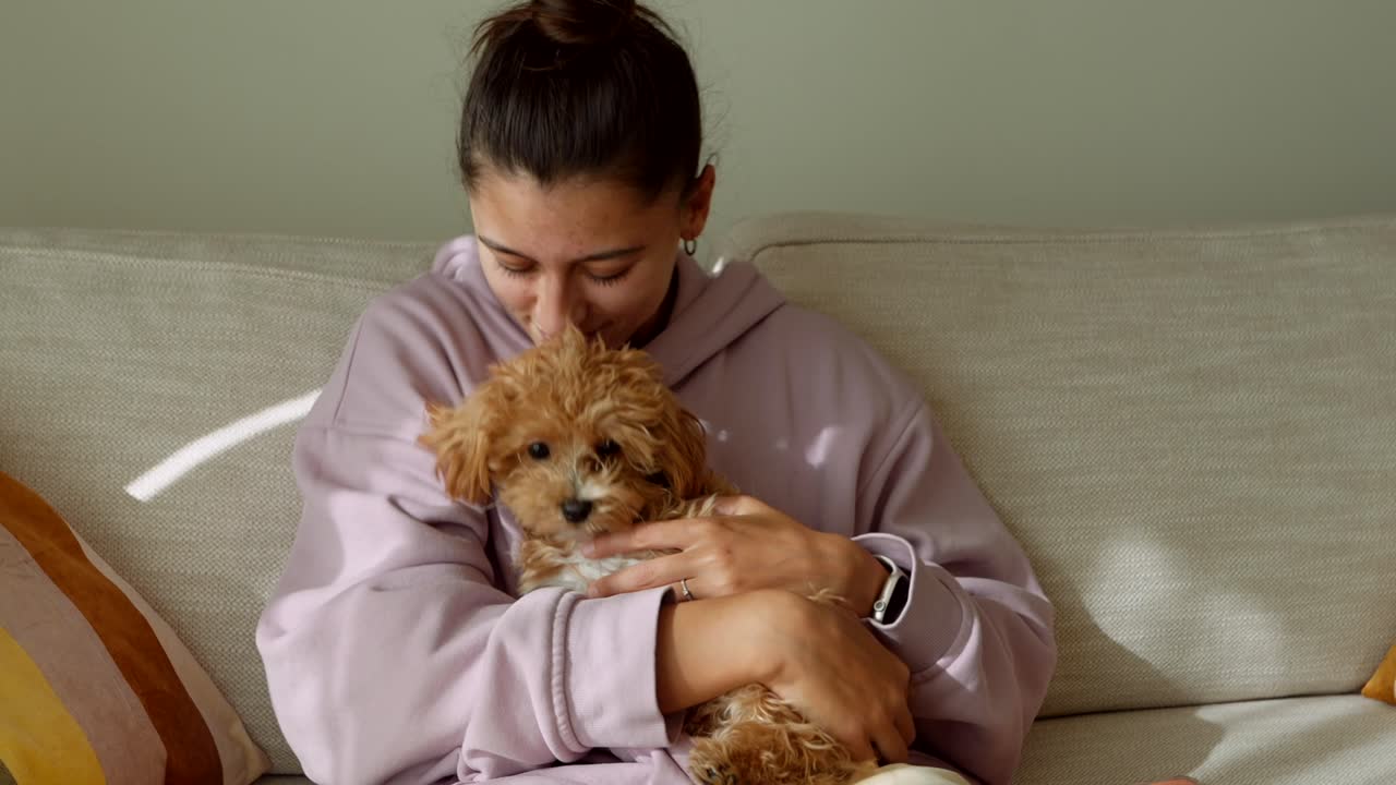 Giovane donna che accarezza e coccola il suo cagnolino felice su un divano
