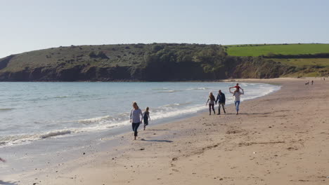 drone shot of multi-generation family on vacation walking along beach by breaking waves