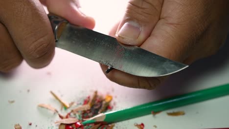 imágenes de manos afilando lentamente un lápiz y algunos lápices de colores con un cuchillo afilado