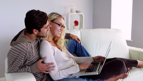 Happy-young-couple-sitting-on-the-couch-using-the-laptop