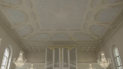 camera pans from the ceiling of a baroque church to the organ and the main entrance