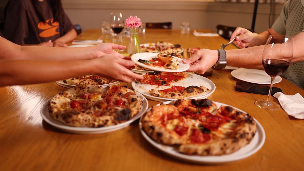 Un gruppo condivide diverse pizze napoletane e vino rosso a un tavolo di legno di un ristorante durante la cena