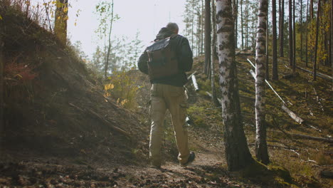 middle-aged-male-hiker-is-walking-alone-in-forest-at-sunny-autumn-day-carrying-backpack-relaxing