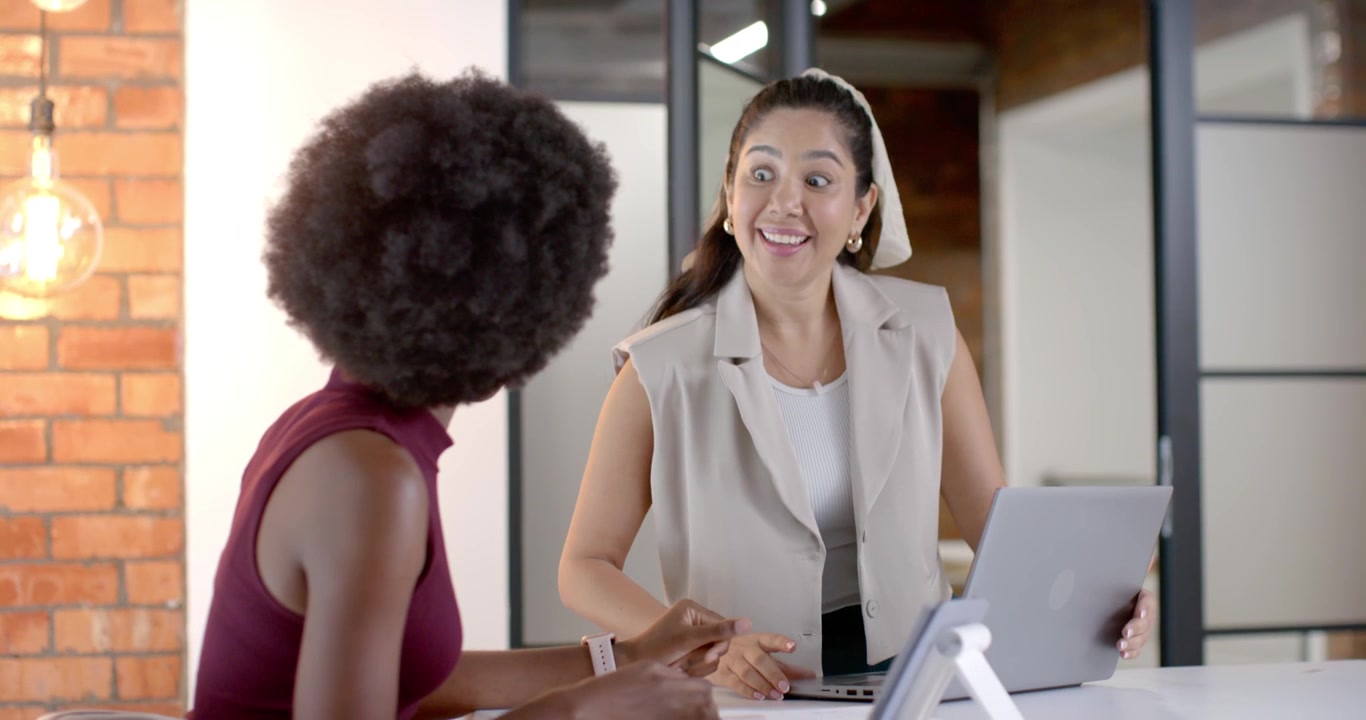 Colegas de trabalho diversas se aproximando, apontando para o laptop na mesa, descobrindo uma ideia e digitando