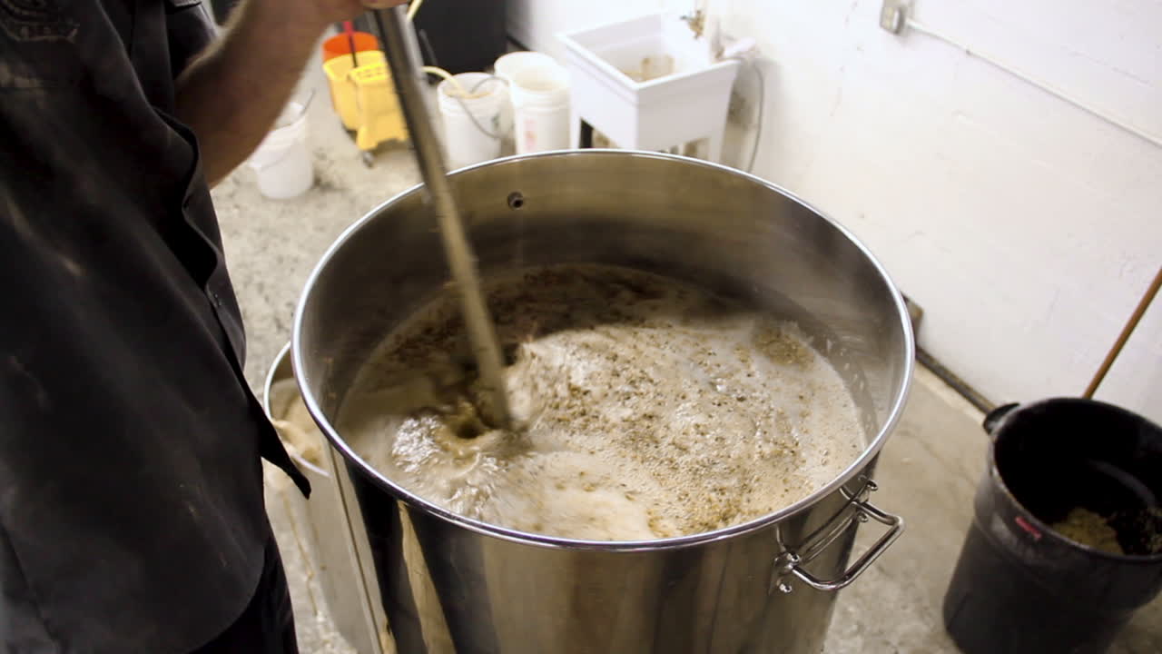 큰 냄비에 밀과 액체를 넣은 신선한 맥주를 붓는 맥주 공장의 노동자