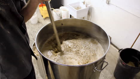 worker in beer factory pouring fresh produced beer with wheat and liquid in large pot