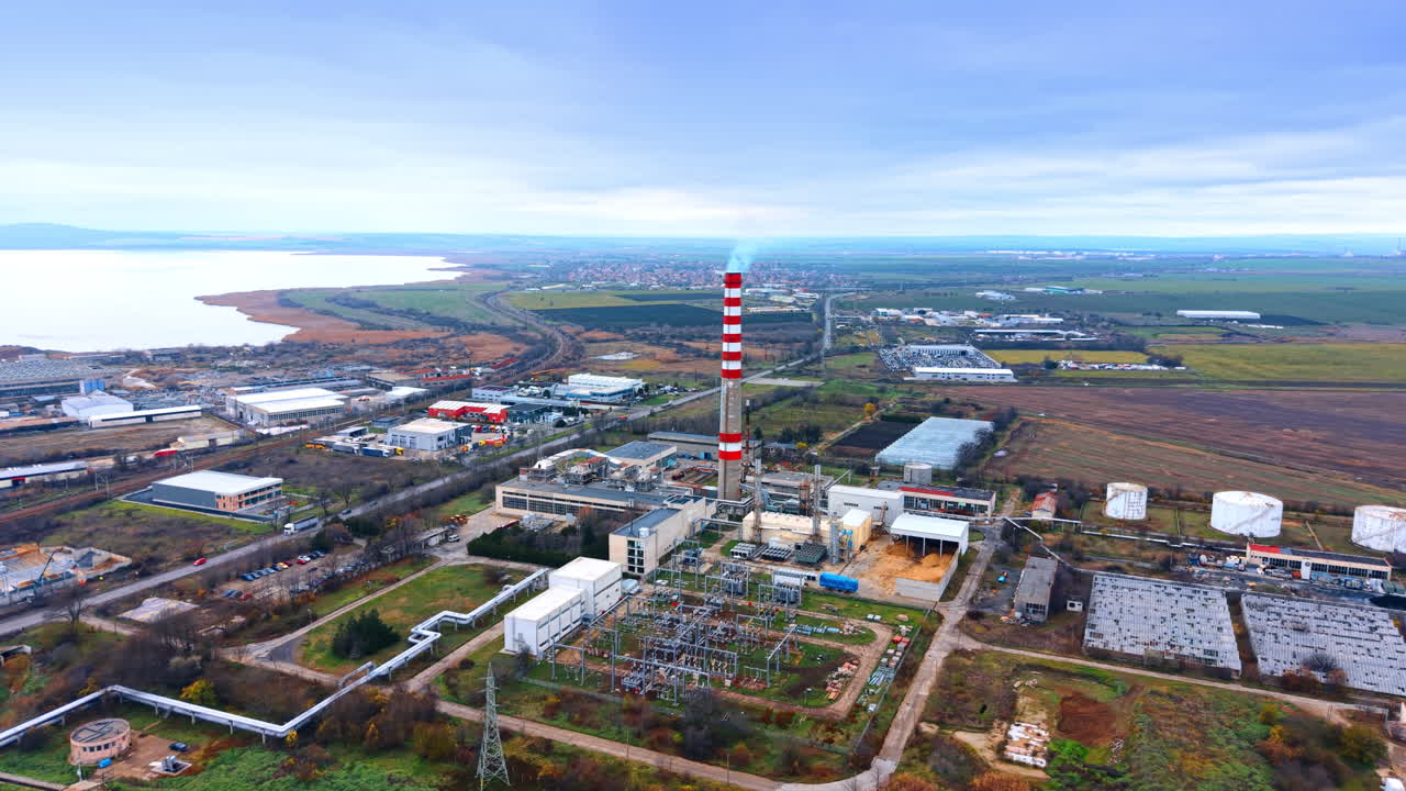 Ampia veduta aerea di zona industriale e centrale elettrica. Veduta panoramica di una centrale termica con camino, pannelli solari e sistemi di raffreddamento vicino a una costa.