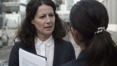 Businesswomen-discussing-papers-on-street