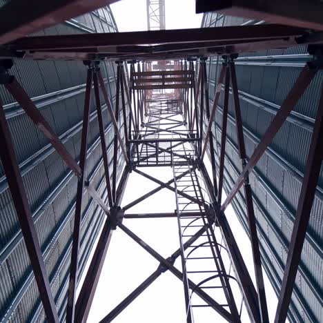 high metal support between two tanks of grain dryer. a walk between the huge tanks right under the metal support. view from below