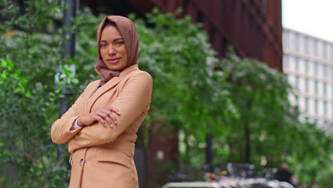 portrait of modern muslim businesswoman wearing hijab with business suit going to work standing outside office buildings folding arms