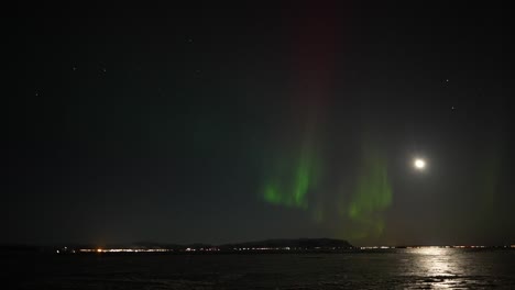 Panning-shot-showing-flickering-red-and-green-northern-lights-over-iced-lake-on-Iceland