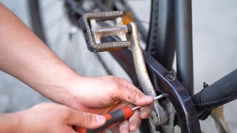 la mano mecánica masculina caucásica usa un destornillador para aflojar el tornillo del pedal de la bicicleta, por encima de la estática de cierre