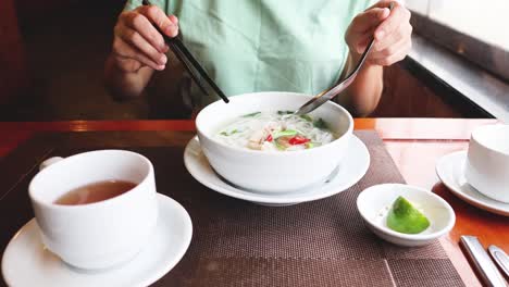 person eating pho and drinking tea at table