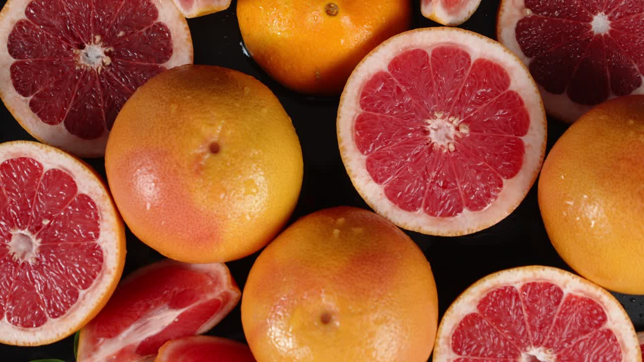 Whole and pieces of fresh grapefruit slowly rotate.