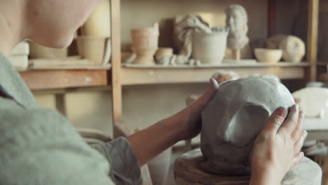 female sculptor modeling clay head with scraper