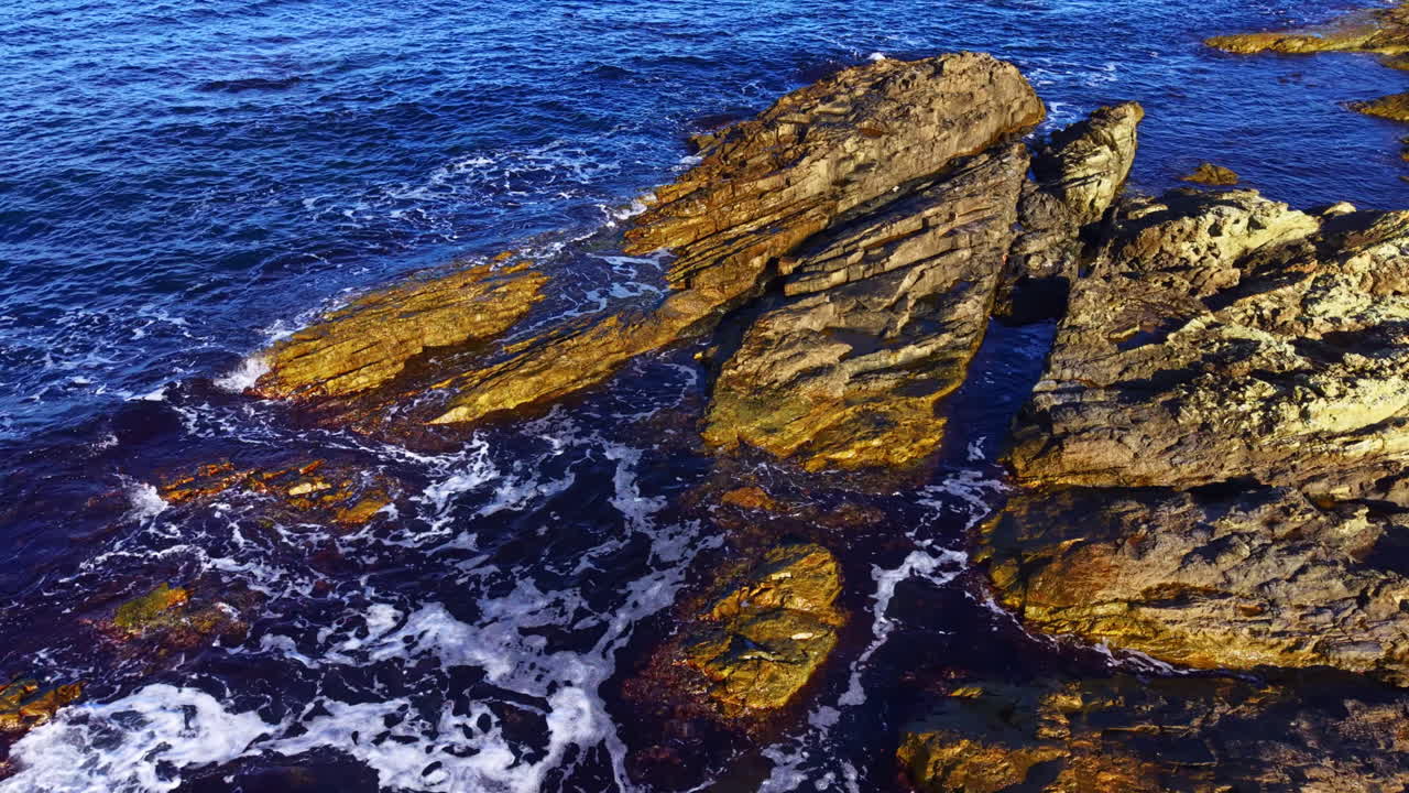Affascinante scena costiera con coste rocciose lambite da dolci onde oceaniche e acque illuminate dal sole al crepuscolo