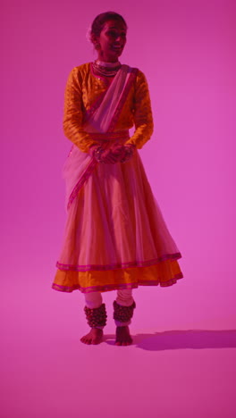 vertical video full length studio shot of female kathak dancer performing dance wearing traditional indian dress against purple background 8